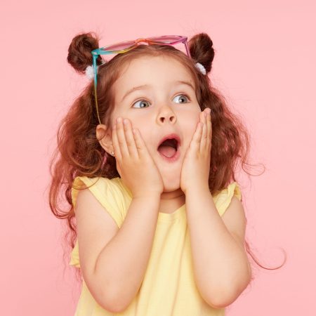 Portrait of surprised cute little toddler girl  in sunglasses over pink background.  Child model have fun and jump. Advertising childrens products